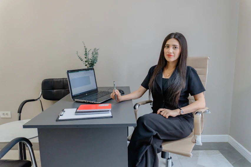 A woman sits at a desk with a laptop.