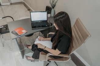 Woman working at a desk with a laptop and notebook.