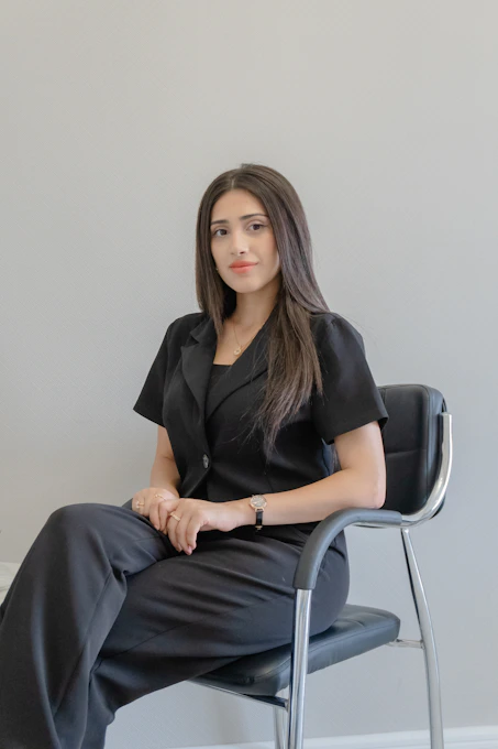 A woman in a black suit sits on a chair.
