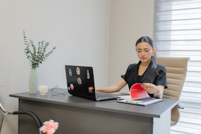 Woman working on laptop at desk with papers.
