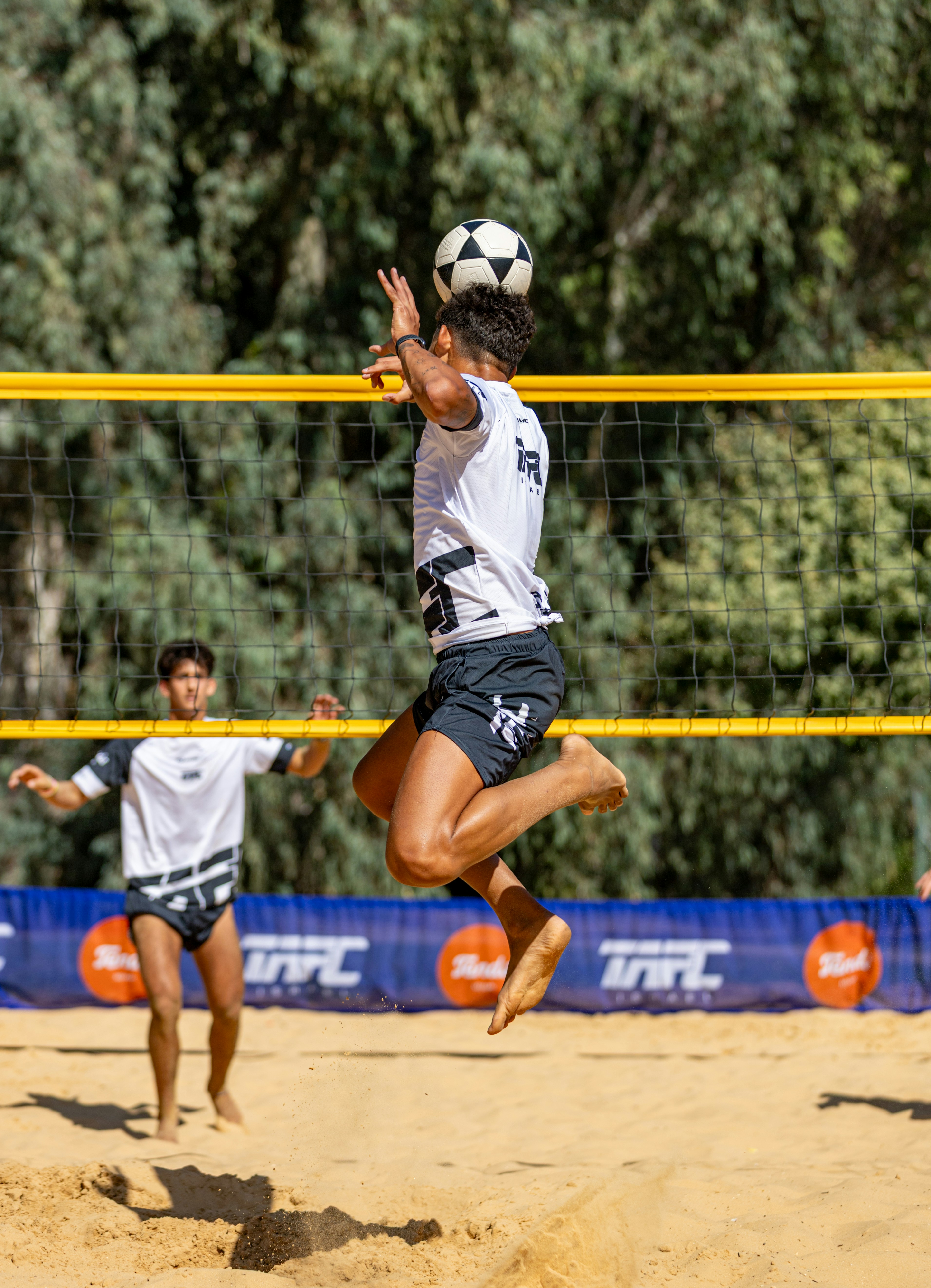 Pria melompat untuk memukul bola sepak di lapangan pantai