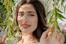 Young woman with dark hair behind green leaves
