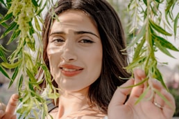 Young woman with dark hair behind green leaves