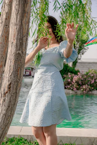 Woman in light blue dress behind tree and beside tree.