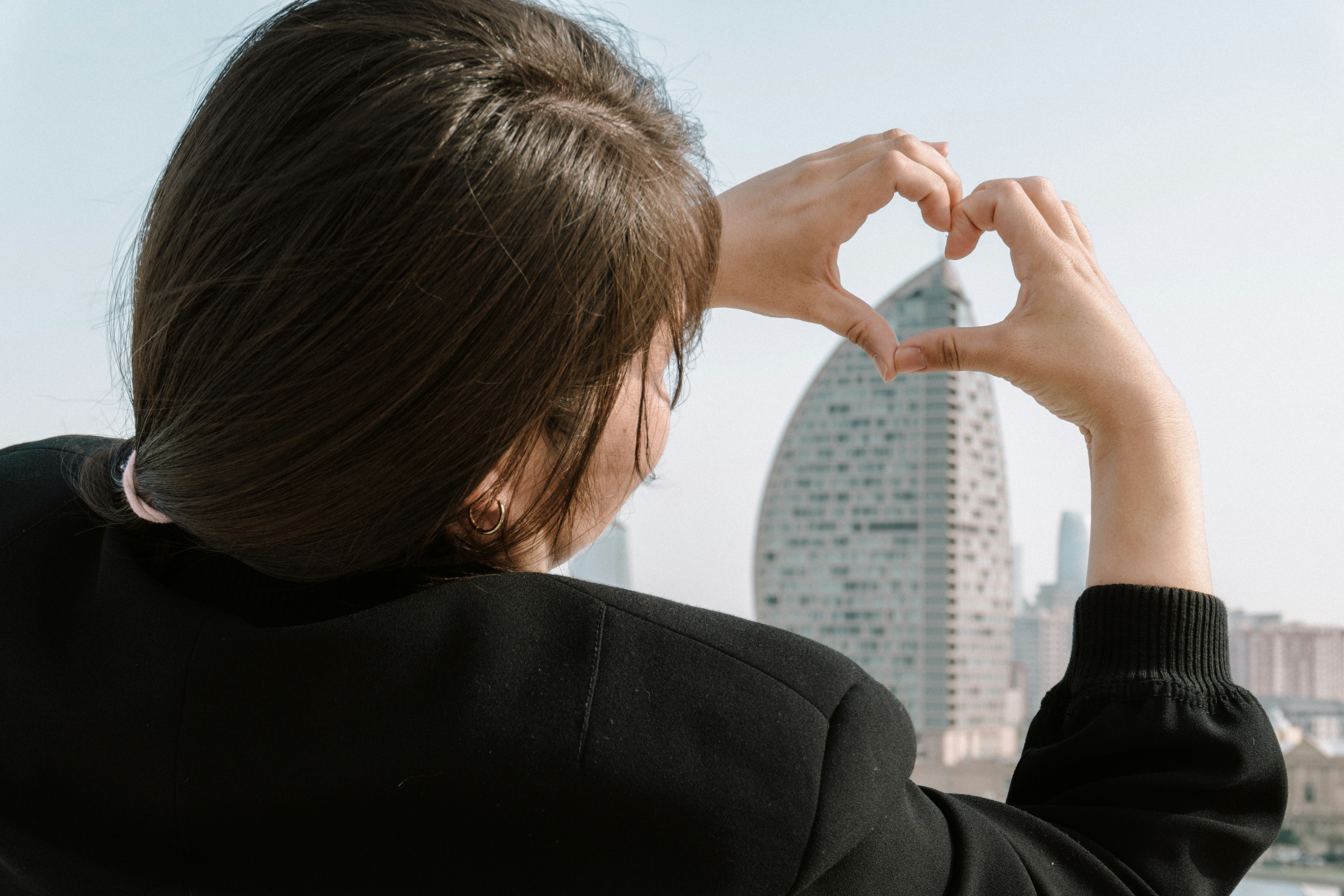 Woman forms heart shape with hands over city buildings