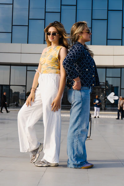 Two young women standing back to back outdoors.