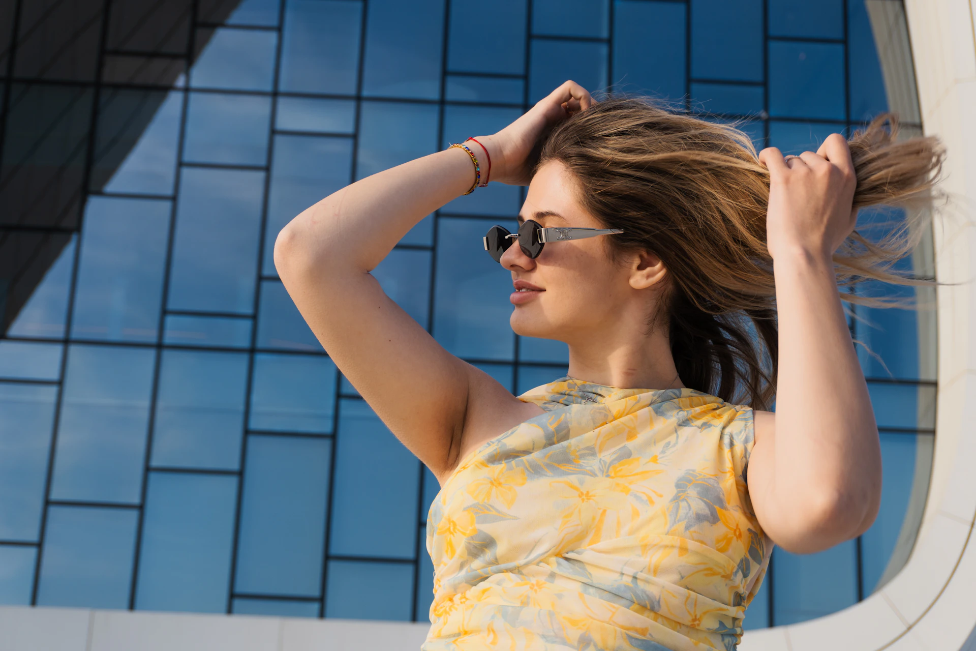 Woman with sunglasses adjusts her blonde hair outdoors.