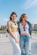 Two young women posing outdoors with cityscape background.