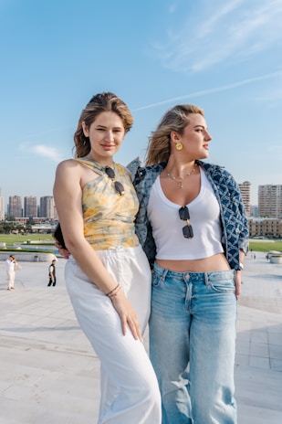 Two young women posing outdoors with cityscape background.