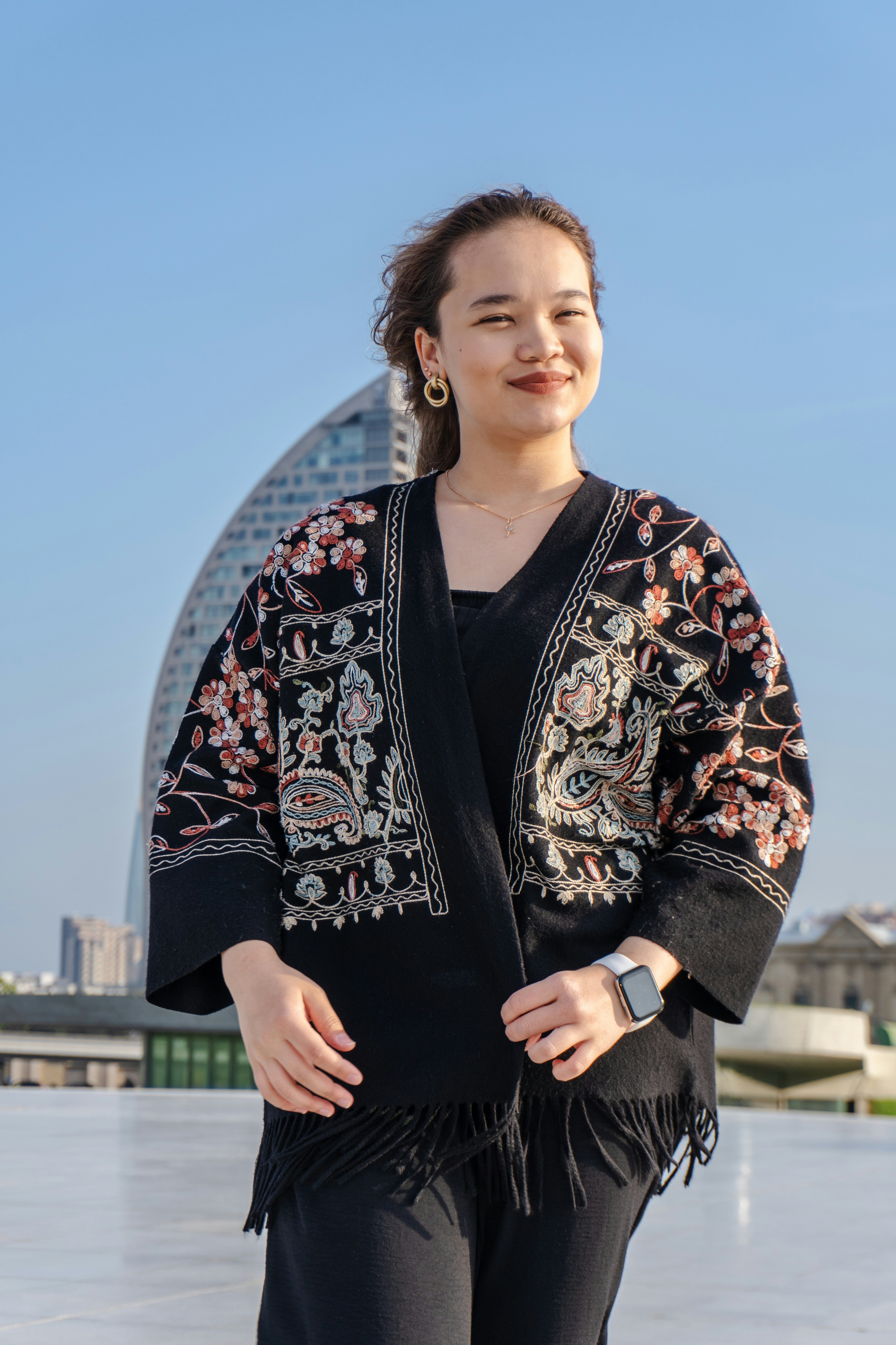 A young woman in a decorative jacket smiles outdoors.