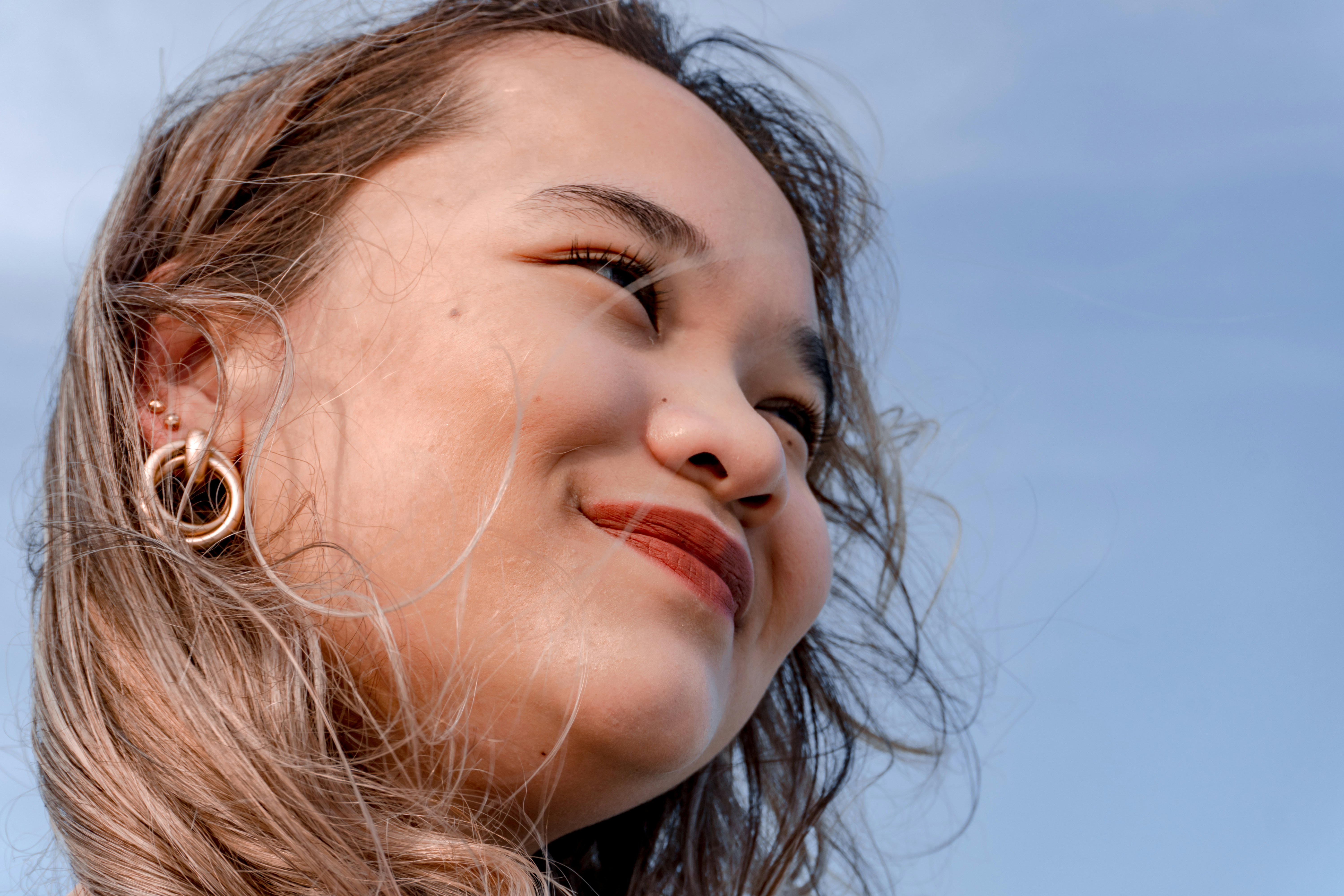 Young woman smiling against a blue sky.
