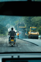 Motorcyclist watches road construction with roller and dump truck.