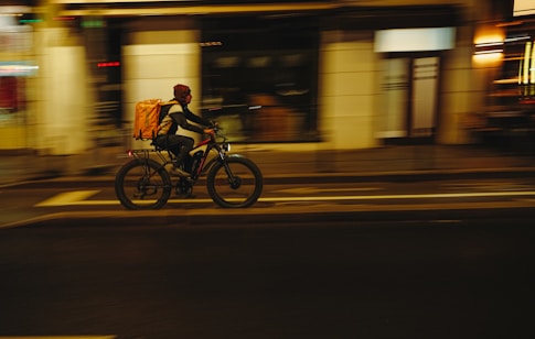 Delivery person rides bicycle through city at night