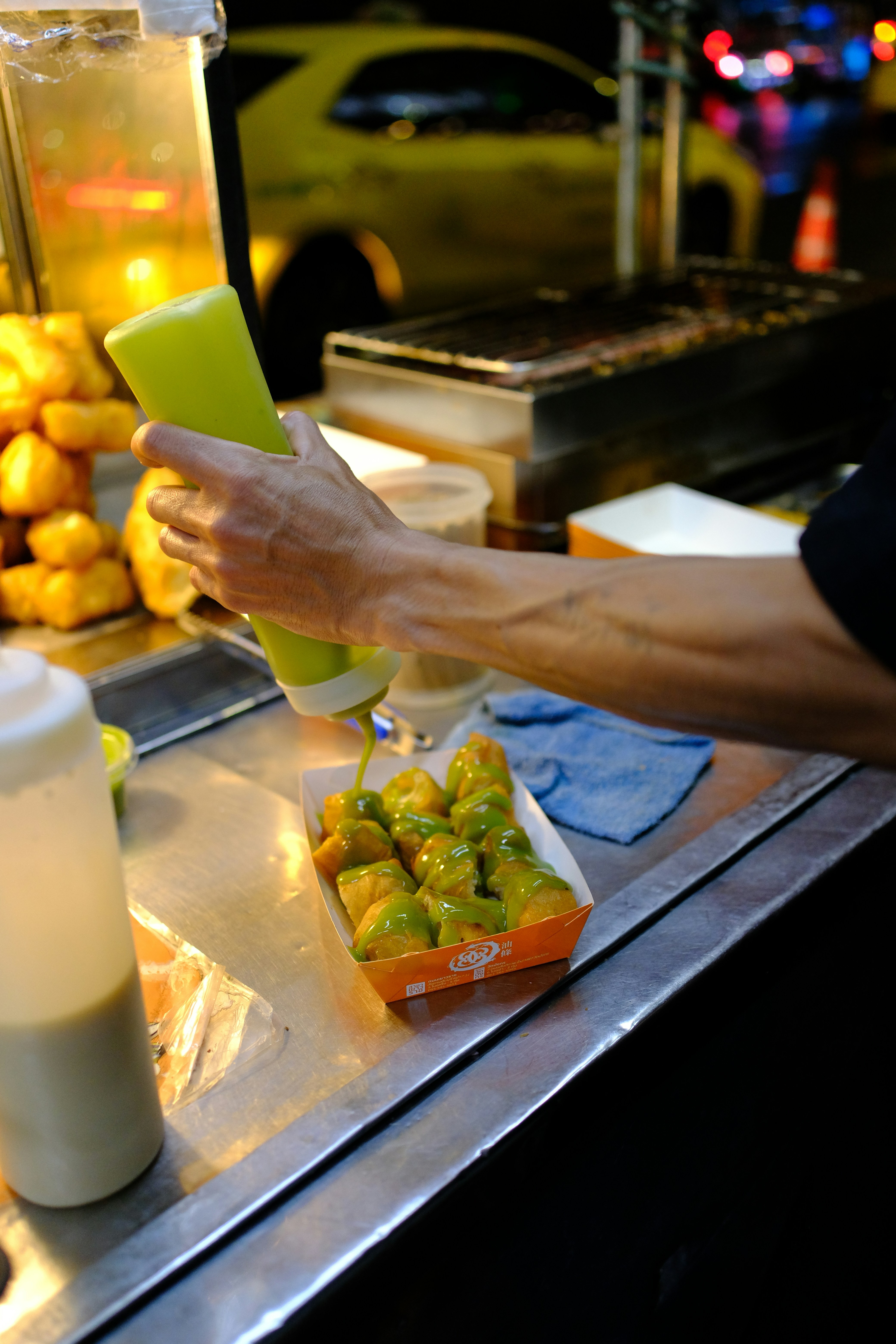 Hand adding sauce to fried food at a street stand.