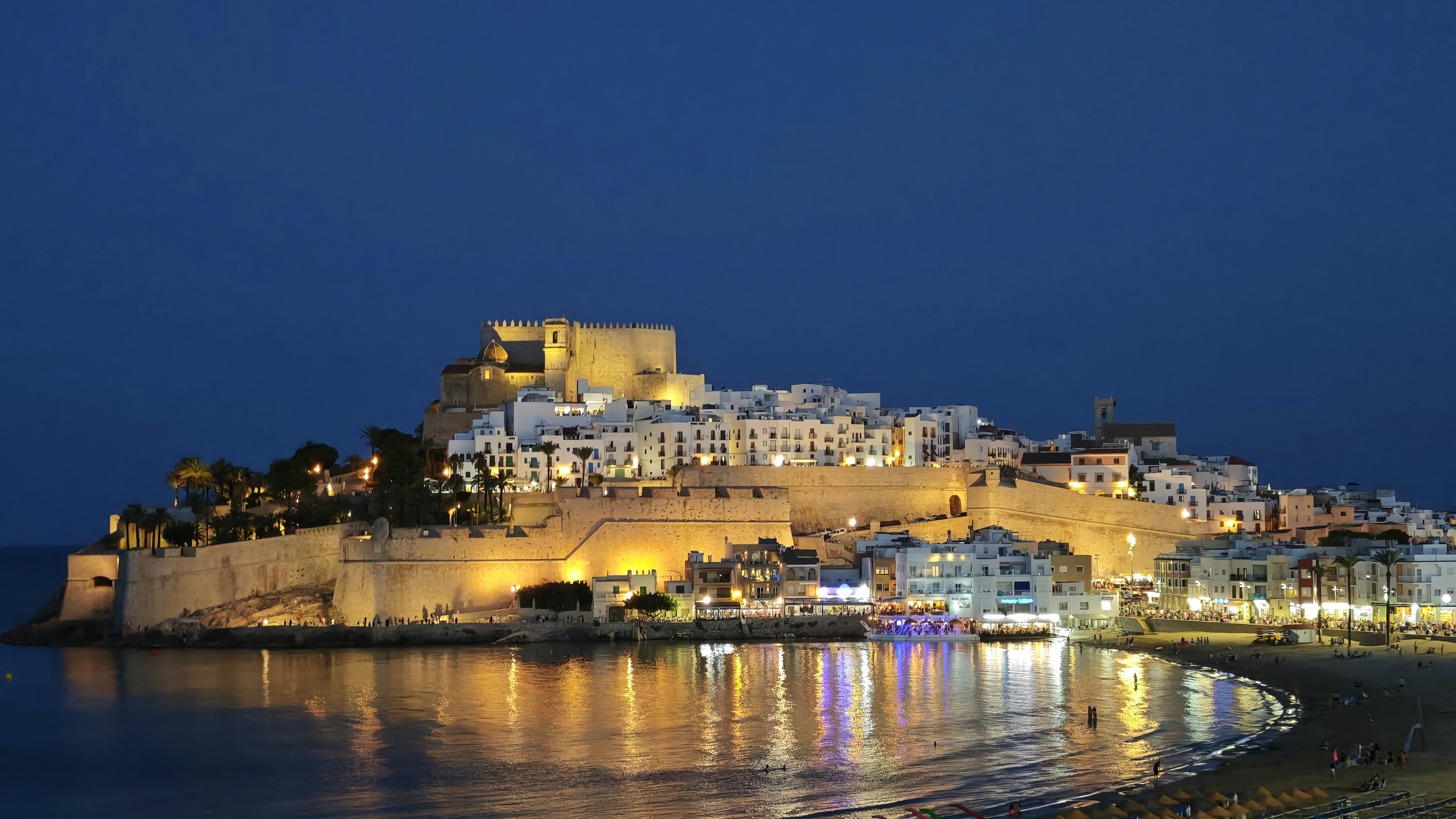 Illuminated coastal town with a castle at night.