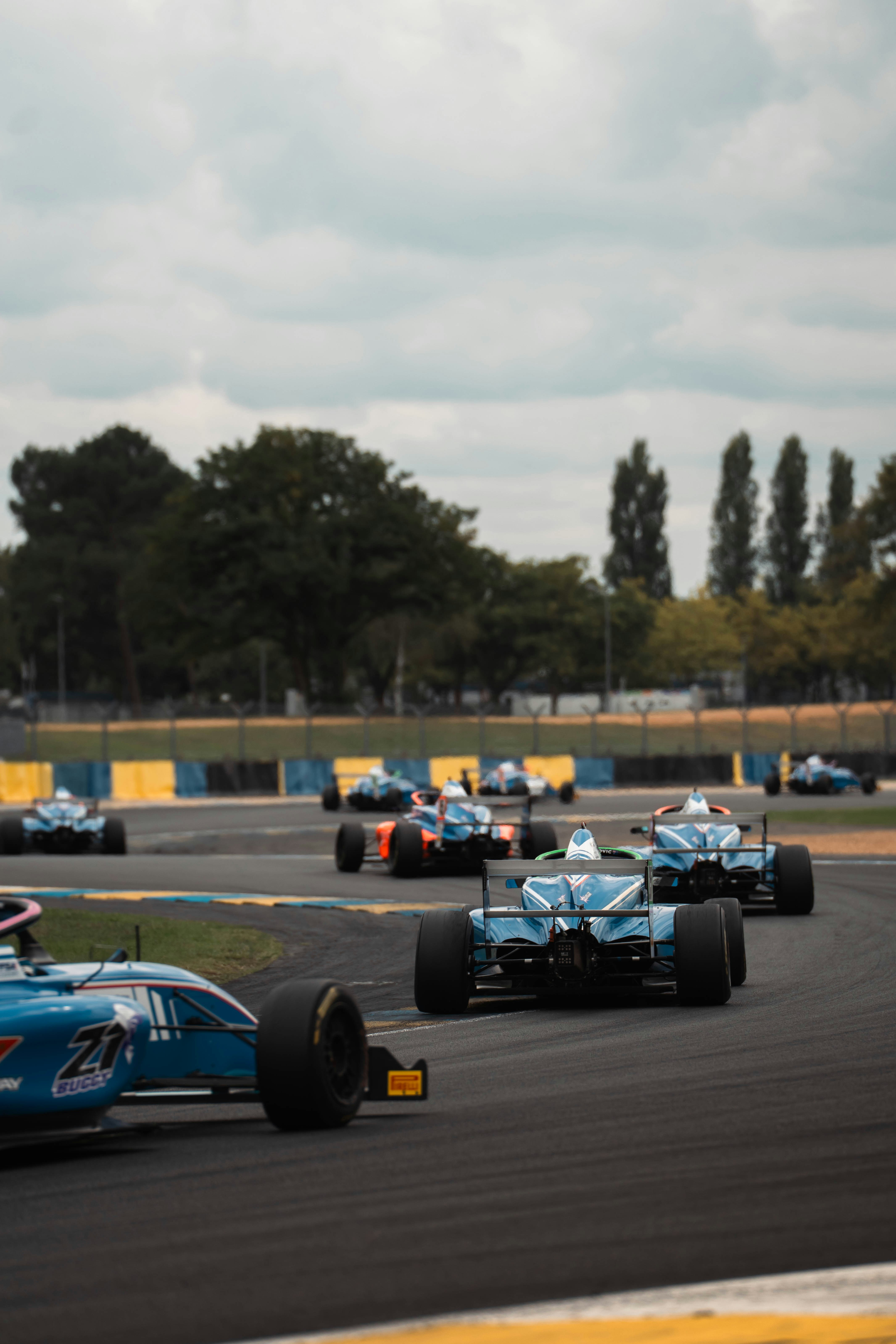 Race cars speeding around a track under cloudy sky.