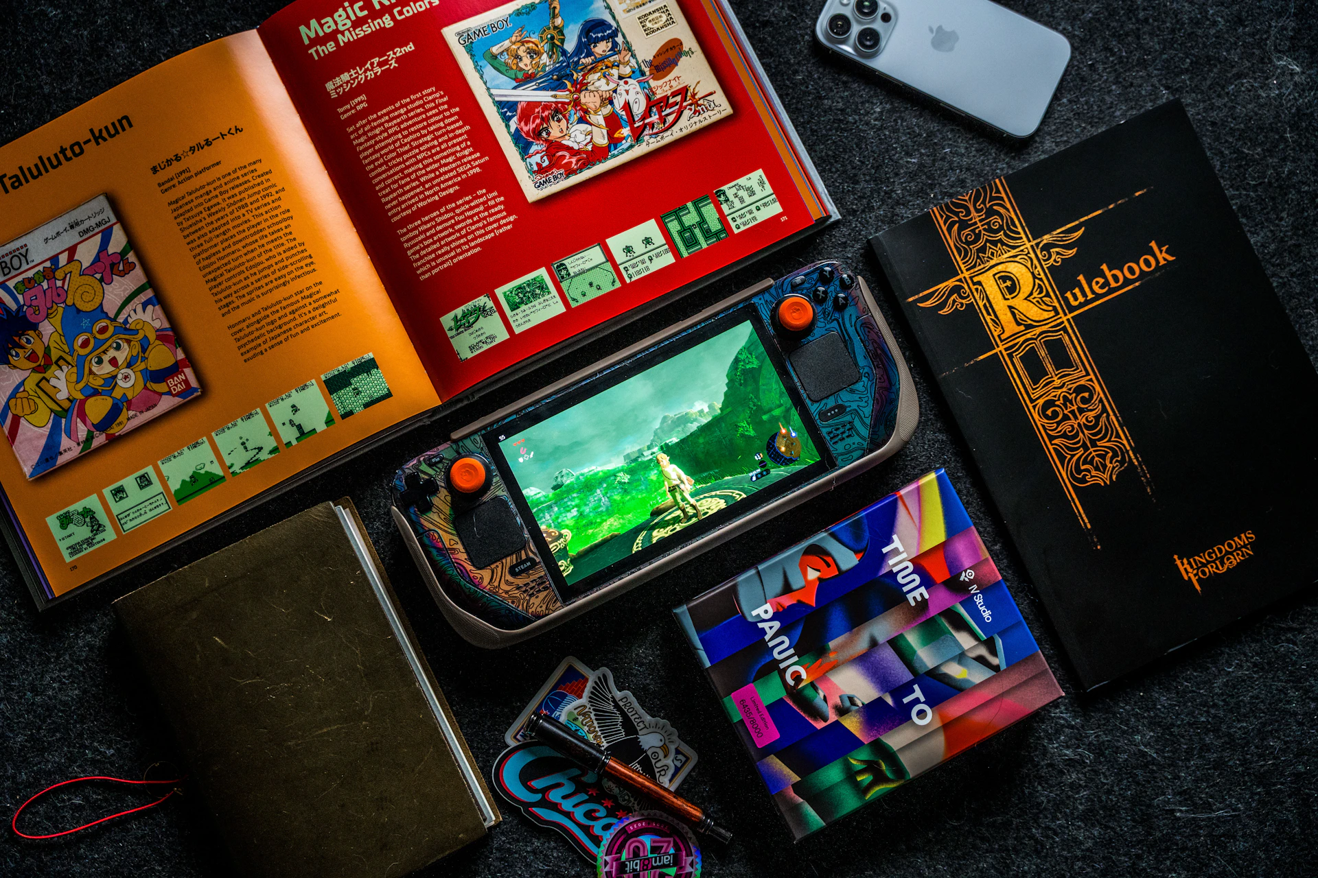 Gaming handheld, books, and phone on dark surface.