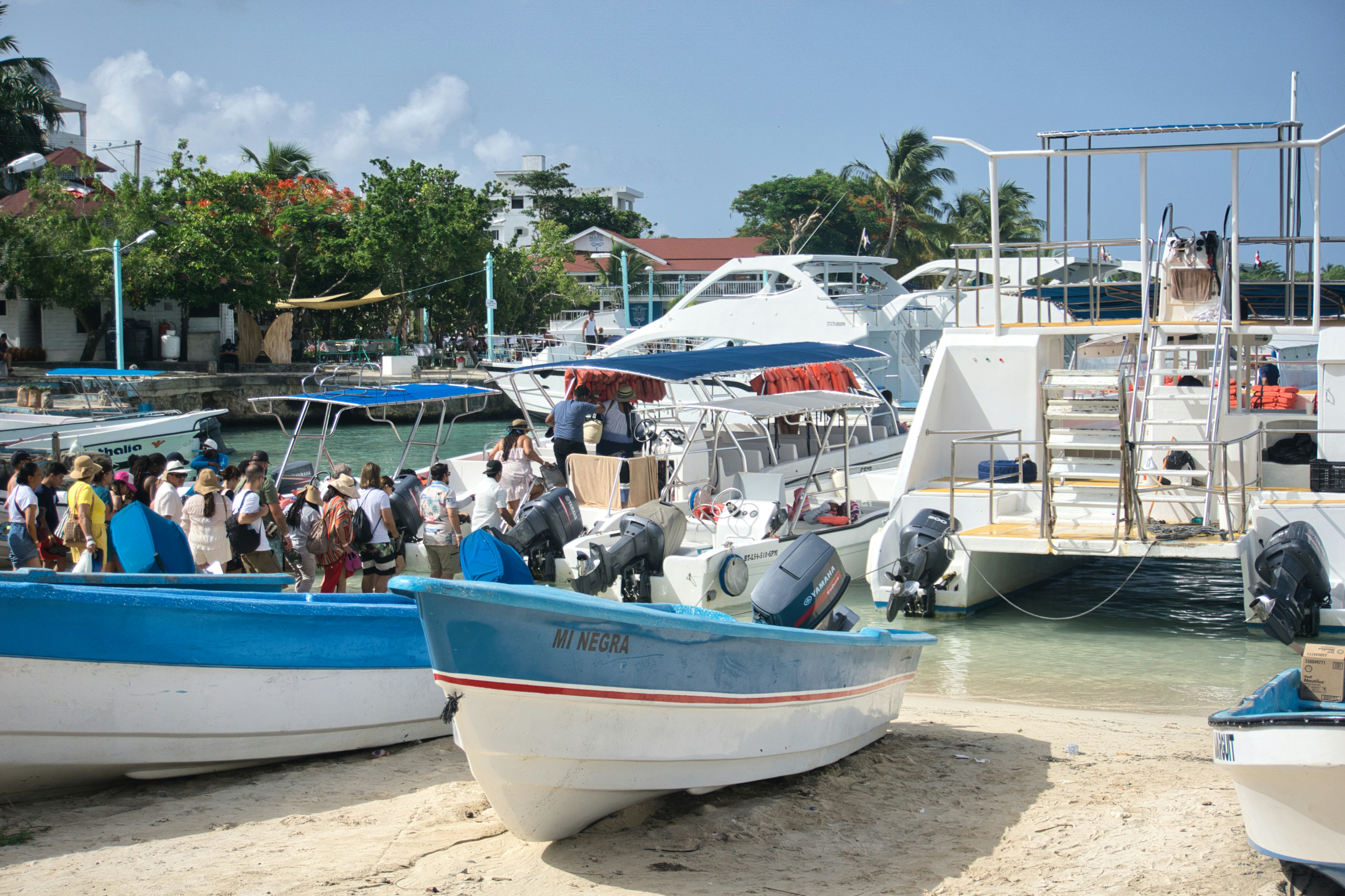 Boats docked at a sunny tropical beach with people