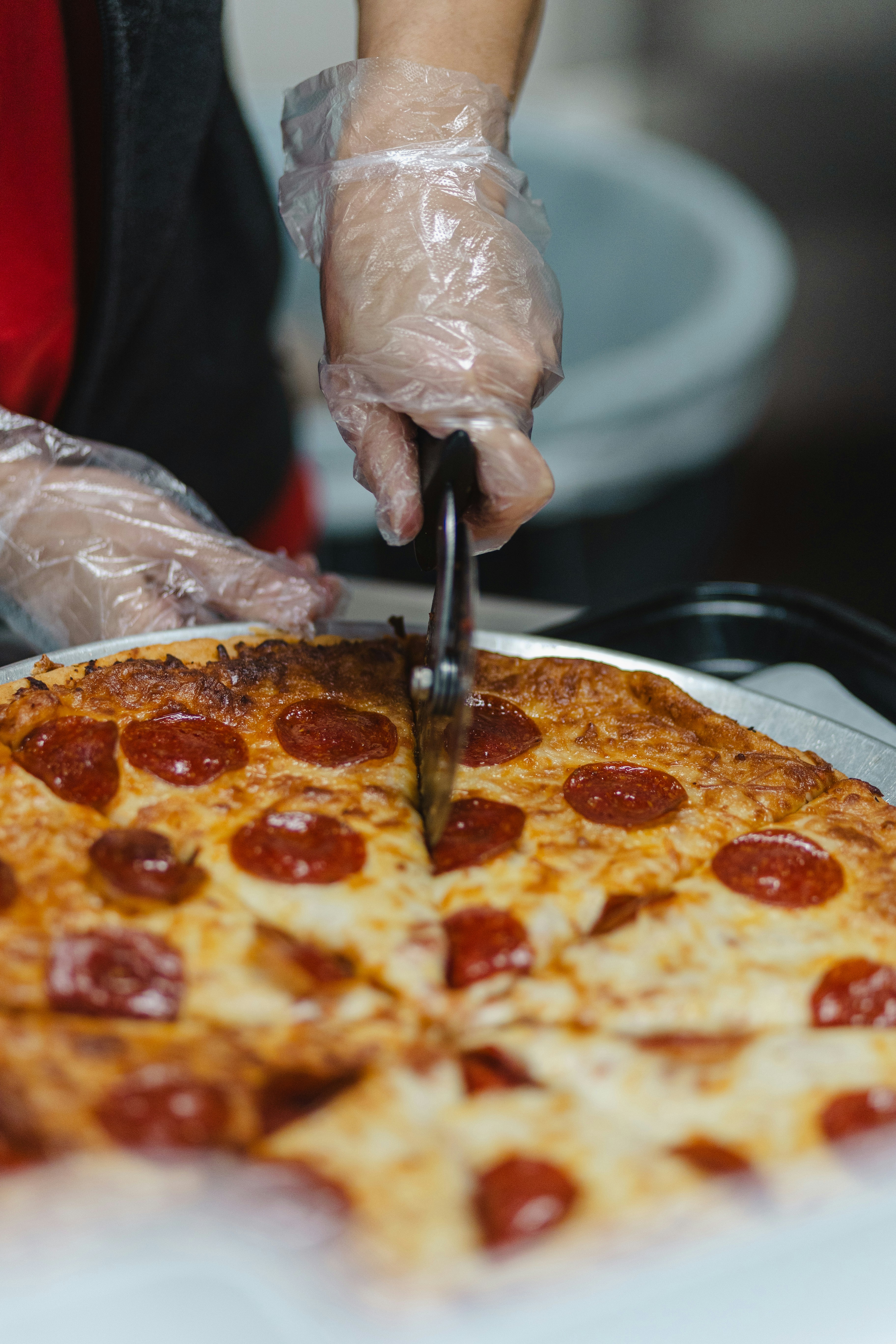 Hands in gloves slicing a pepperoni pizza.