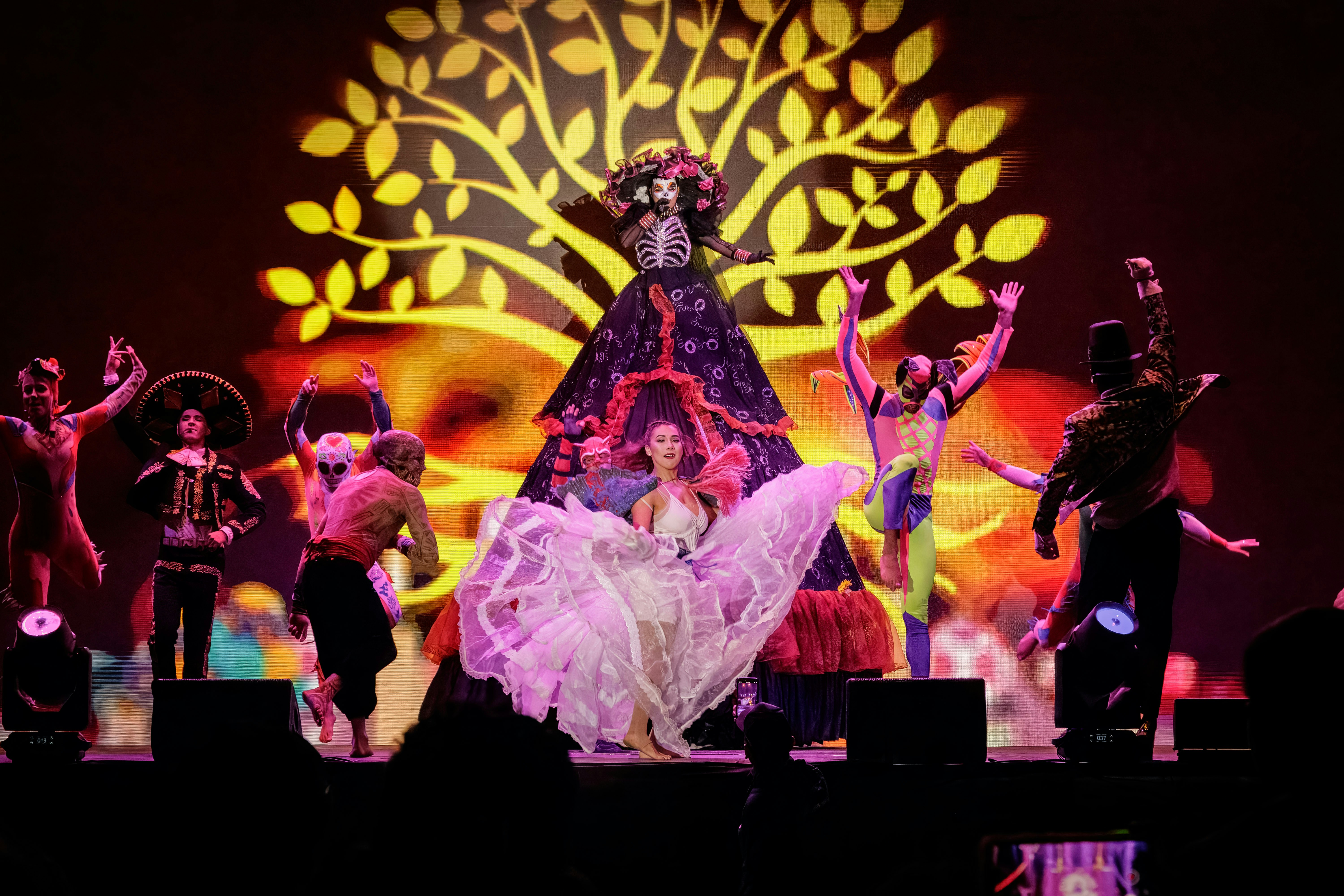 Dancers perform on stage with a large tree projection.