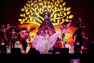 Dancers perform on stage with a large tree projection.