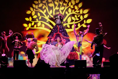 Dancers perform on stage with a large tree projection.