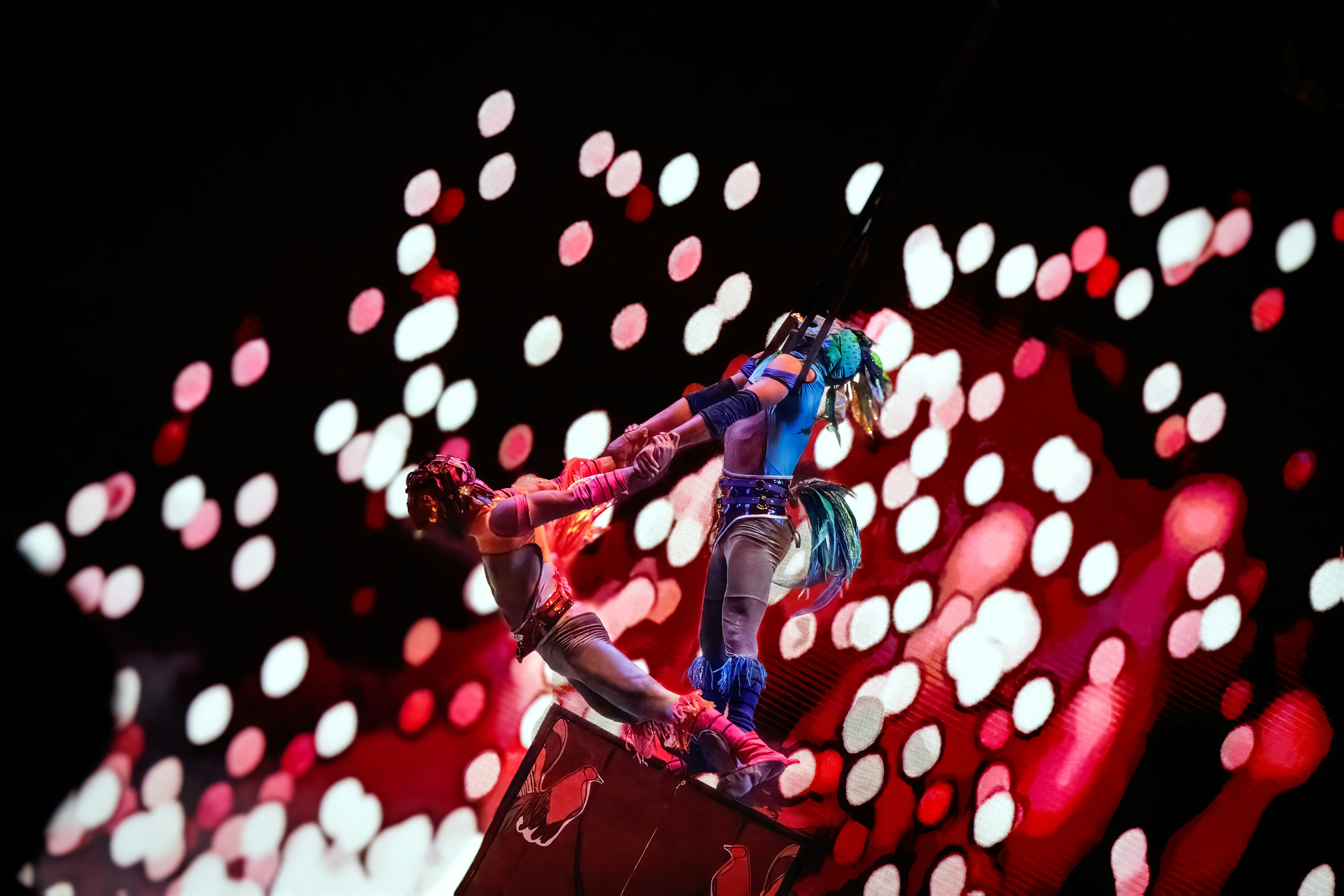 Two acrobats perform on a stage with abstract lights.