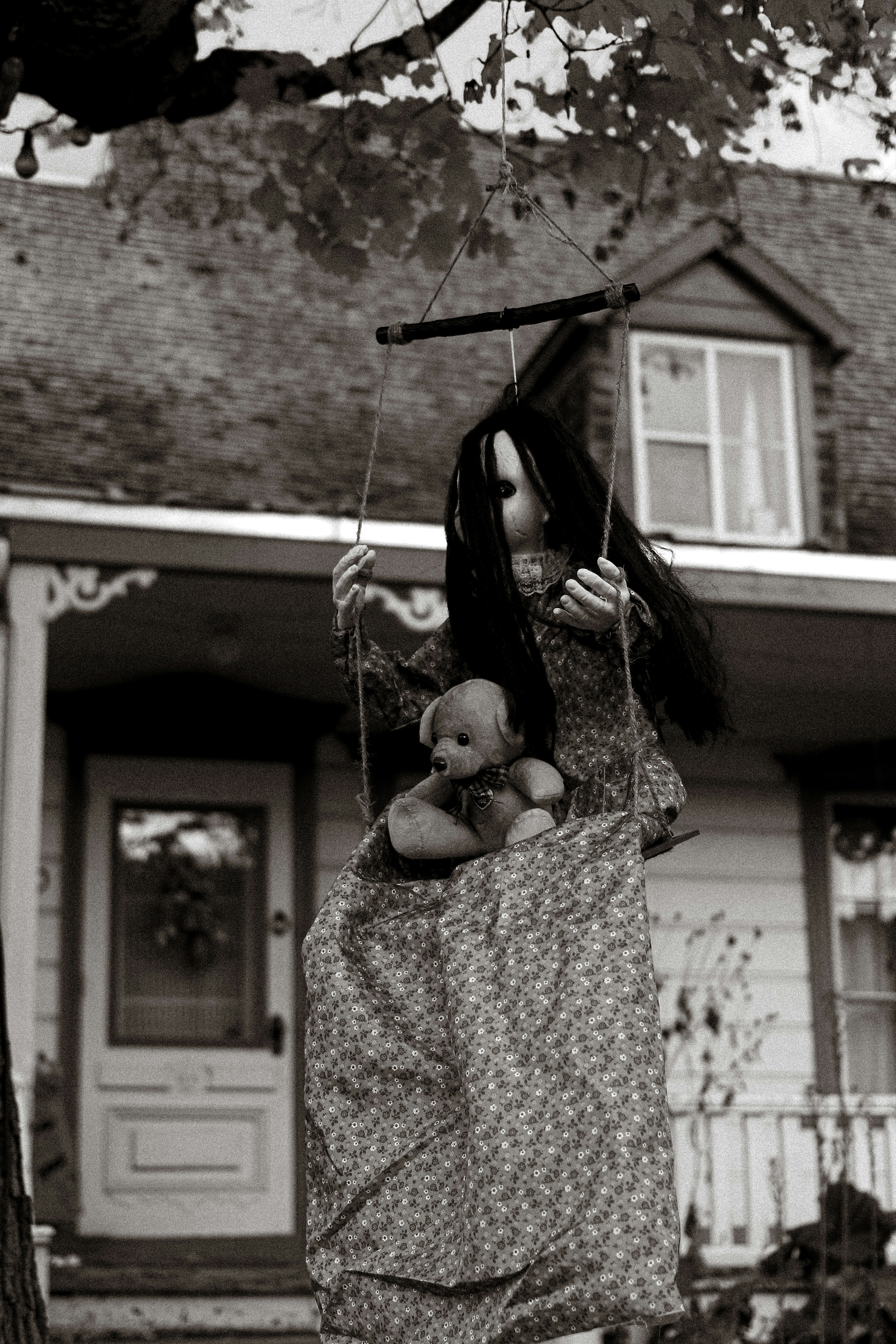 Creepy doll on swing with teddy bear in yard