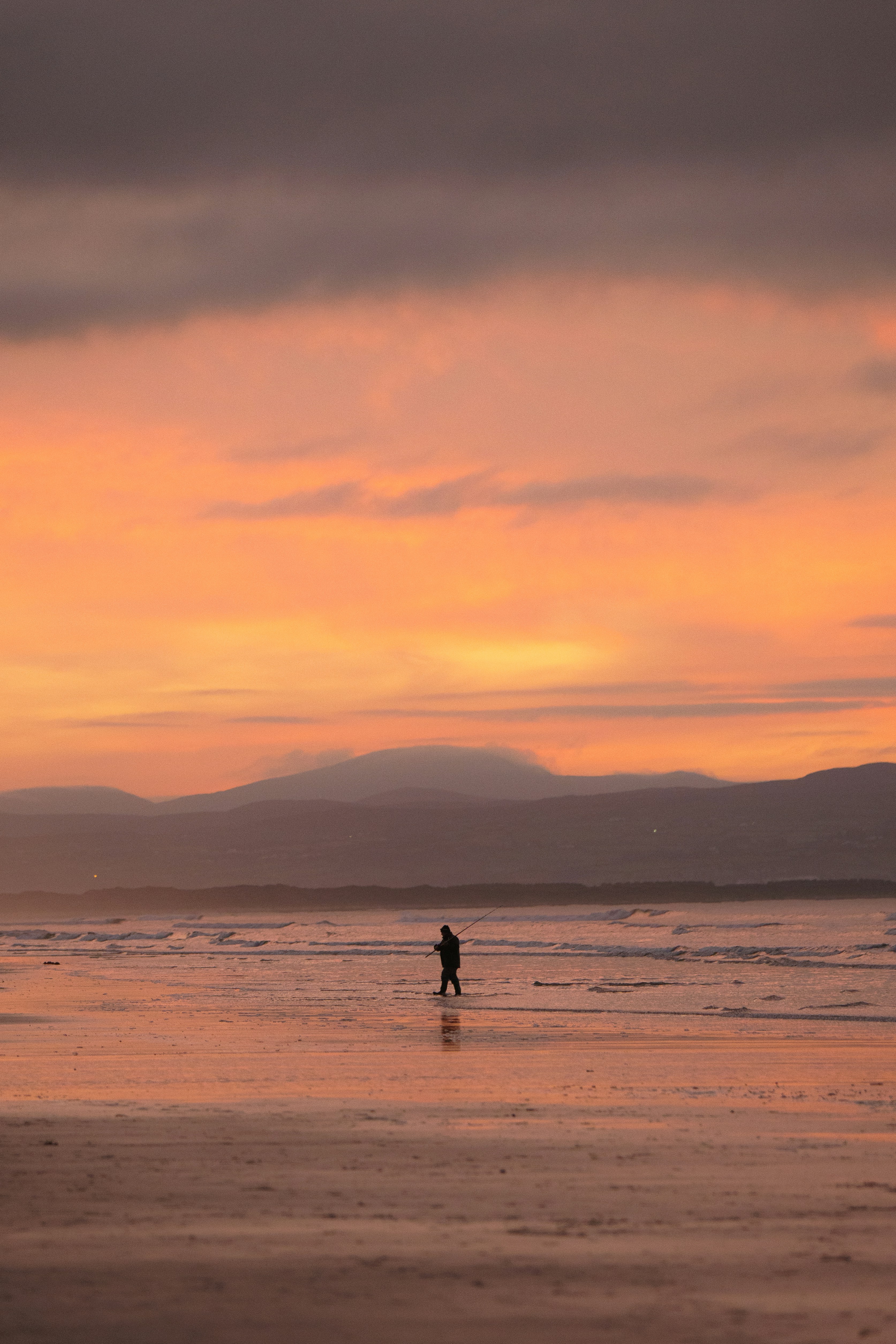 A lone figure walks on a beach at sunset.