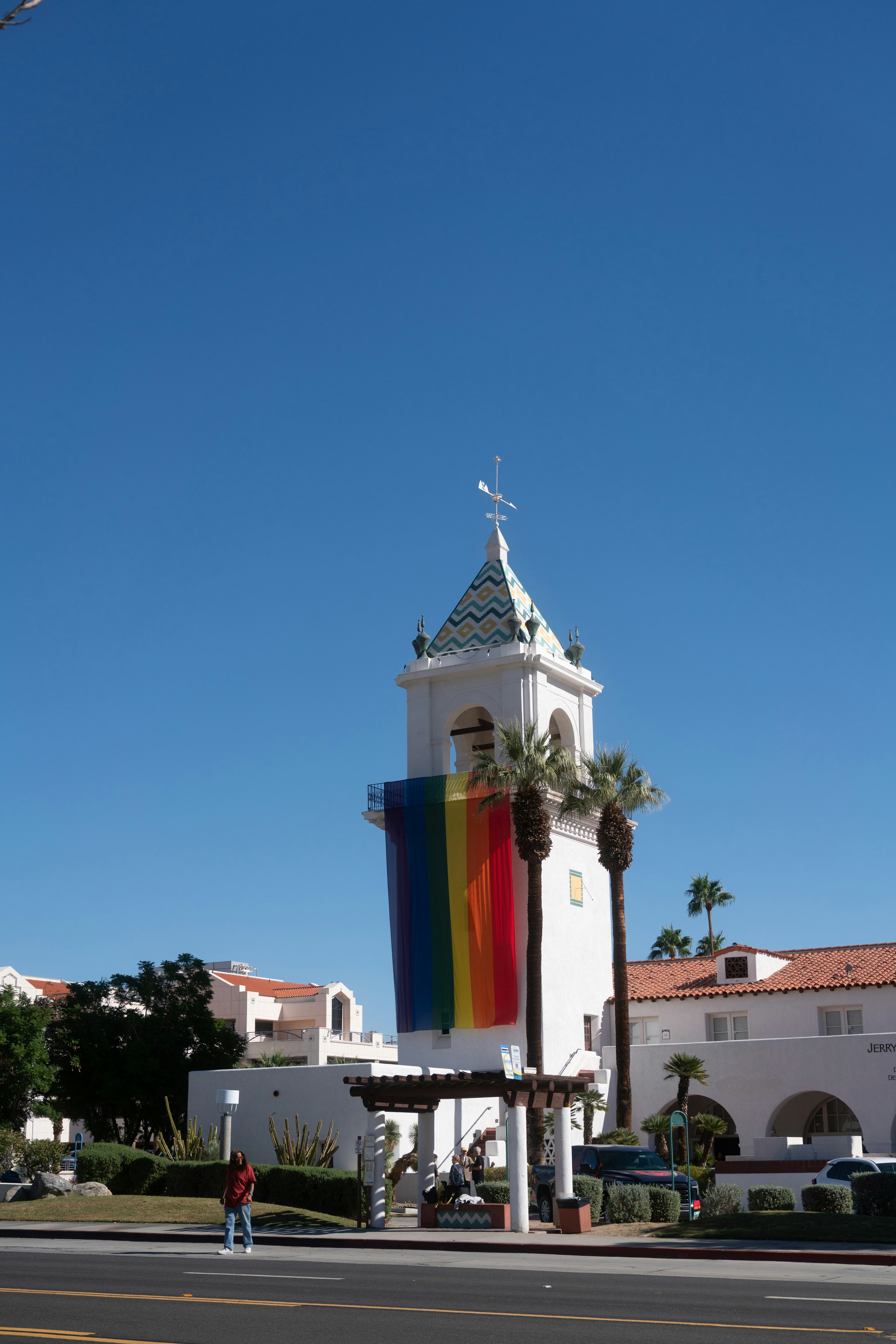 Weißer Turm mit Regenbogenflagge und Palmen.