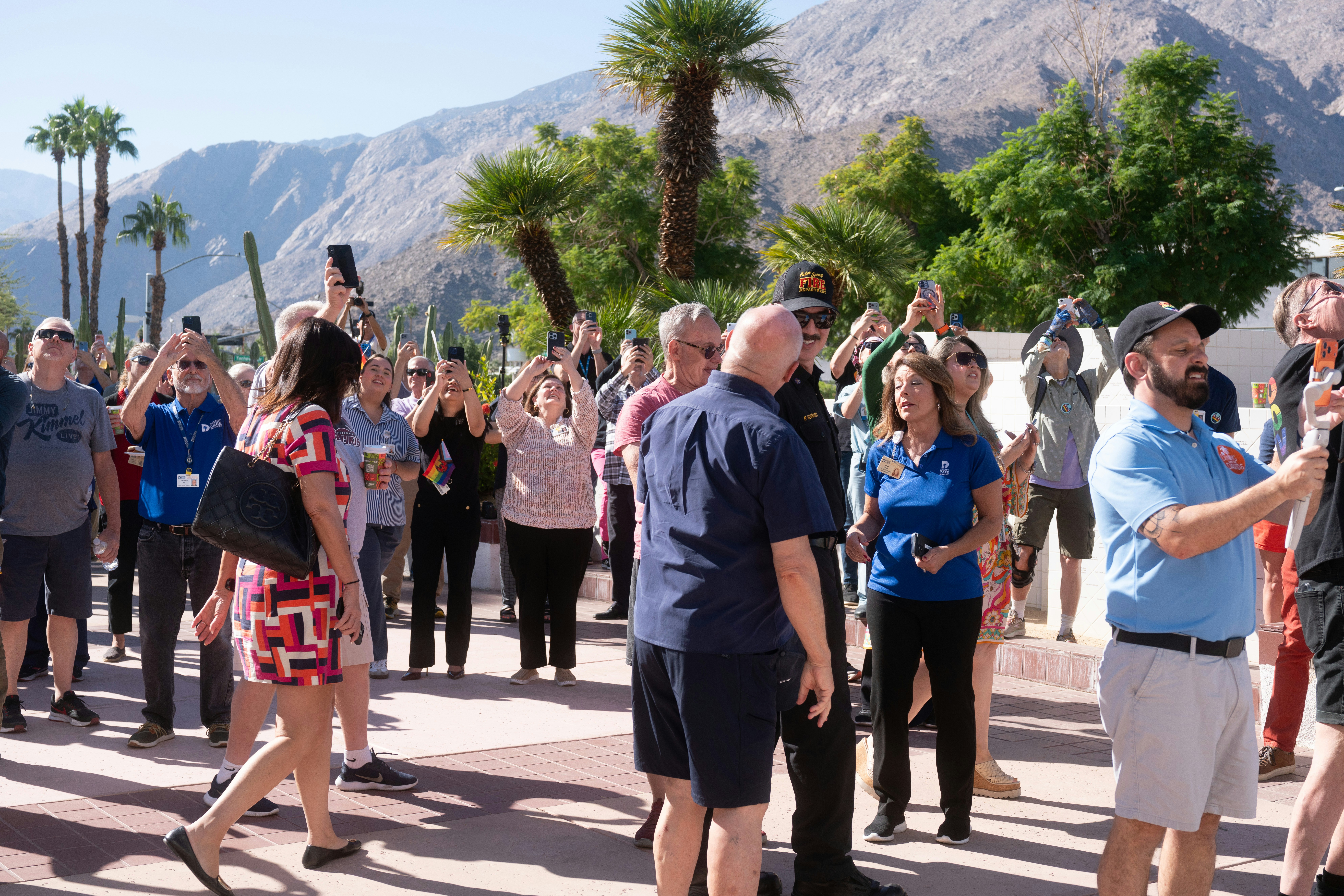 Crowd gathers outdoors, holding up phones to capture something.