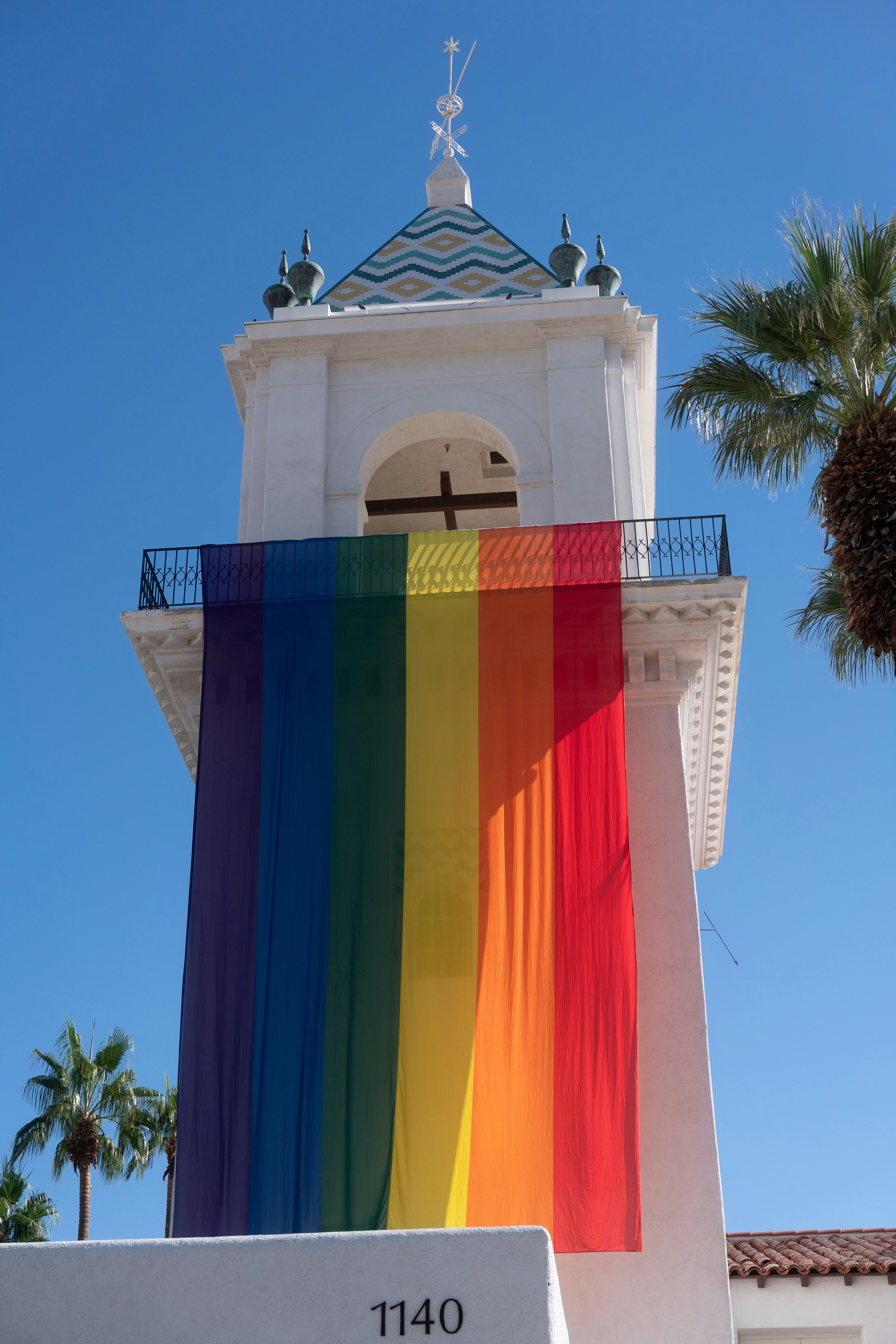 Weißer Glockenturm mit Regenbogenflagge und Palmen