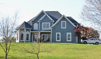 A large blue house sits on a grassy hill.