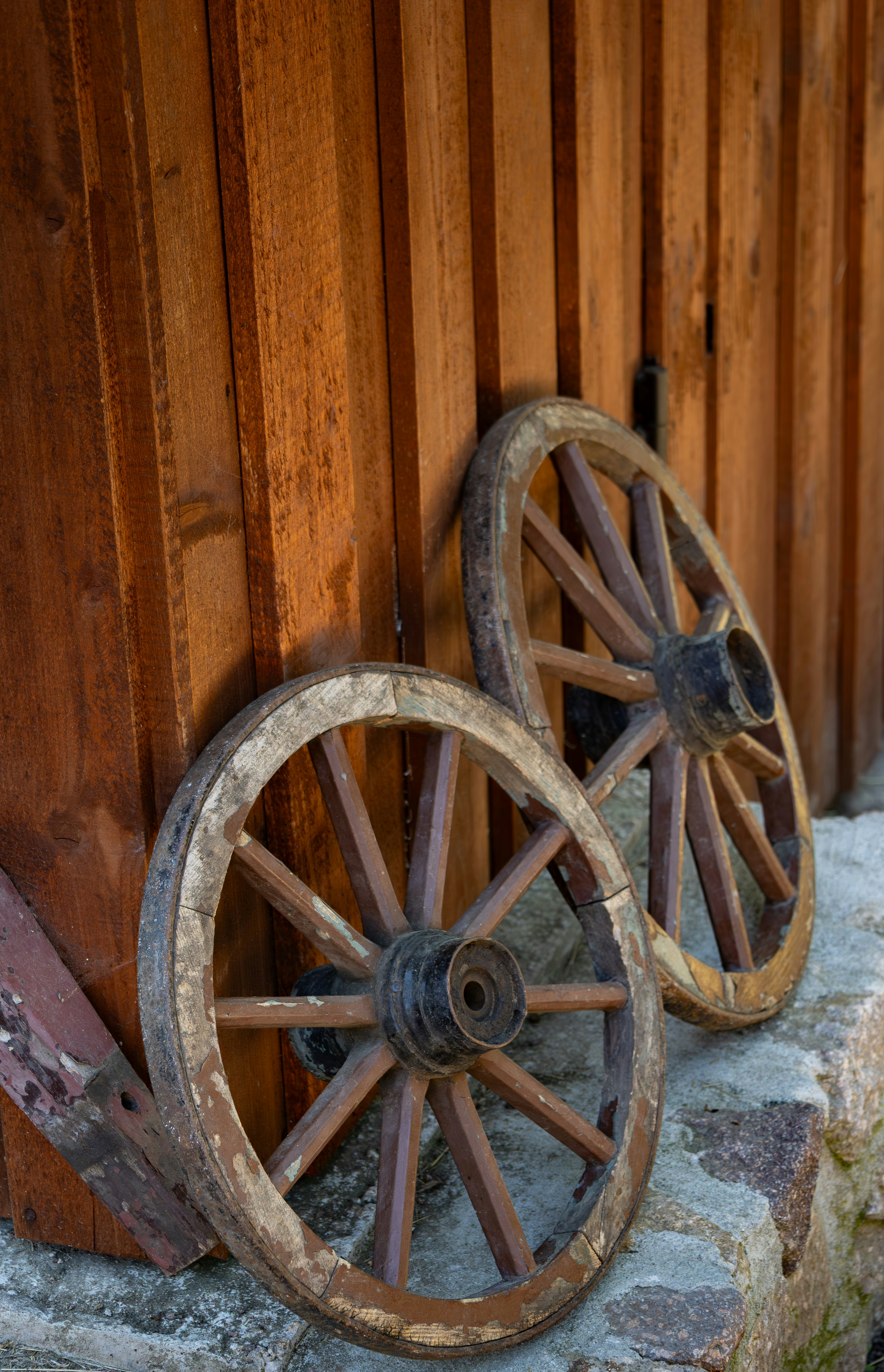 Two old wooden wagon wheels leaning against wall.
