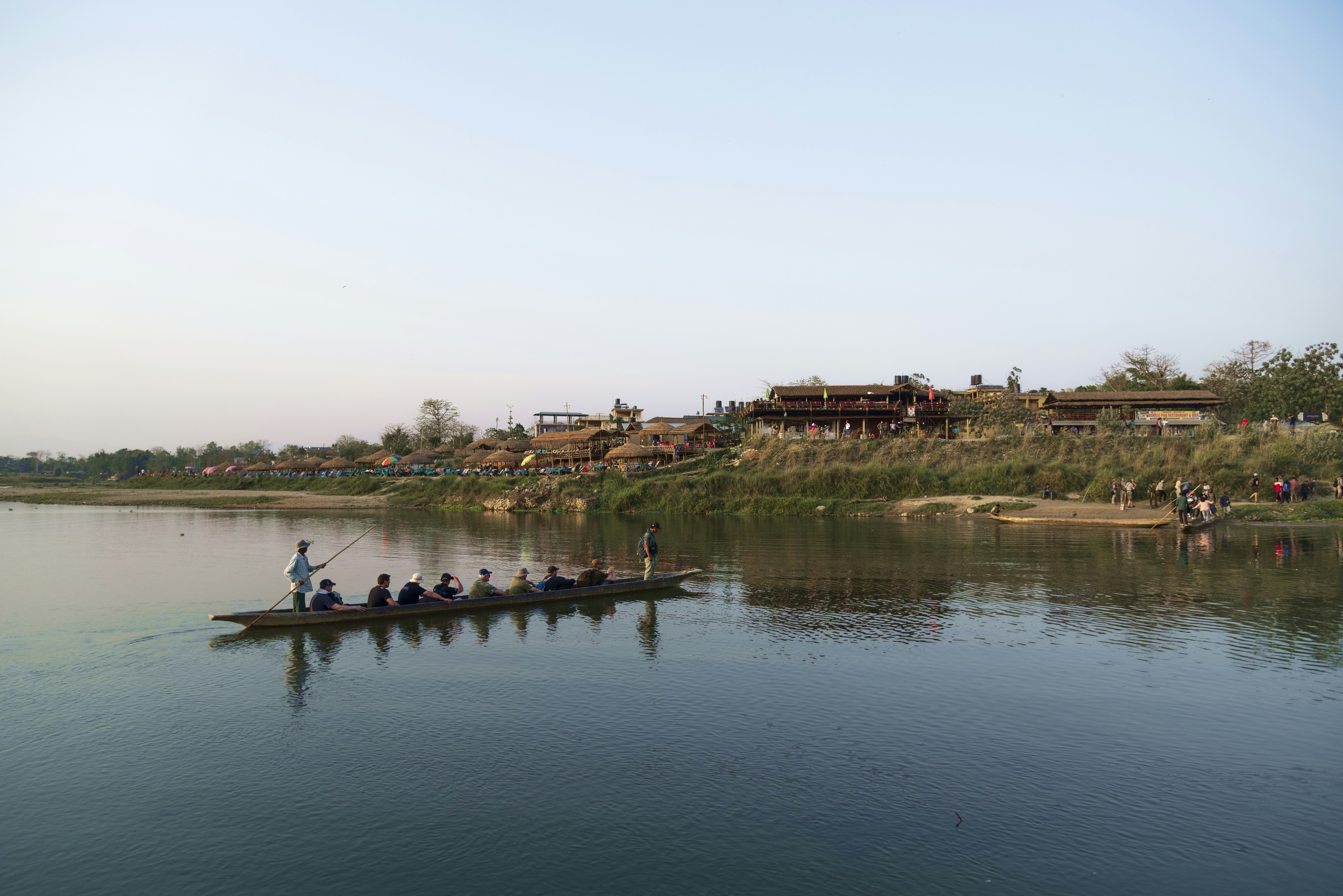 People riding a long boat on a wide river.