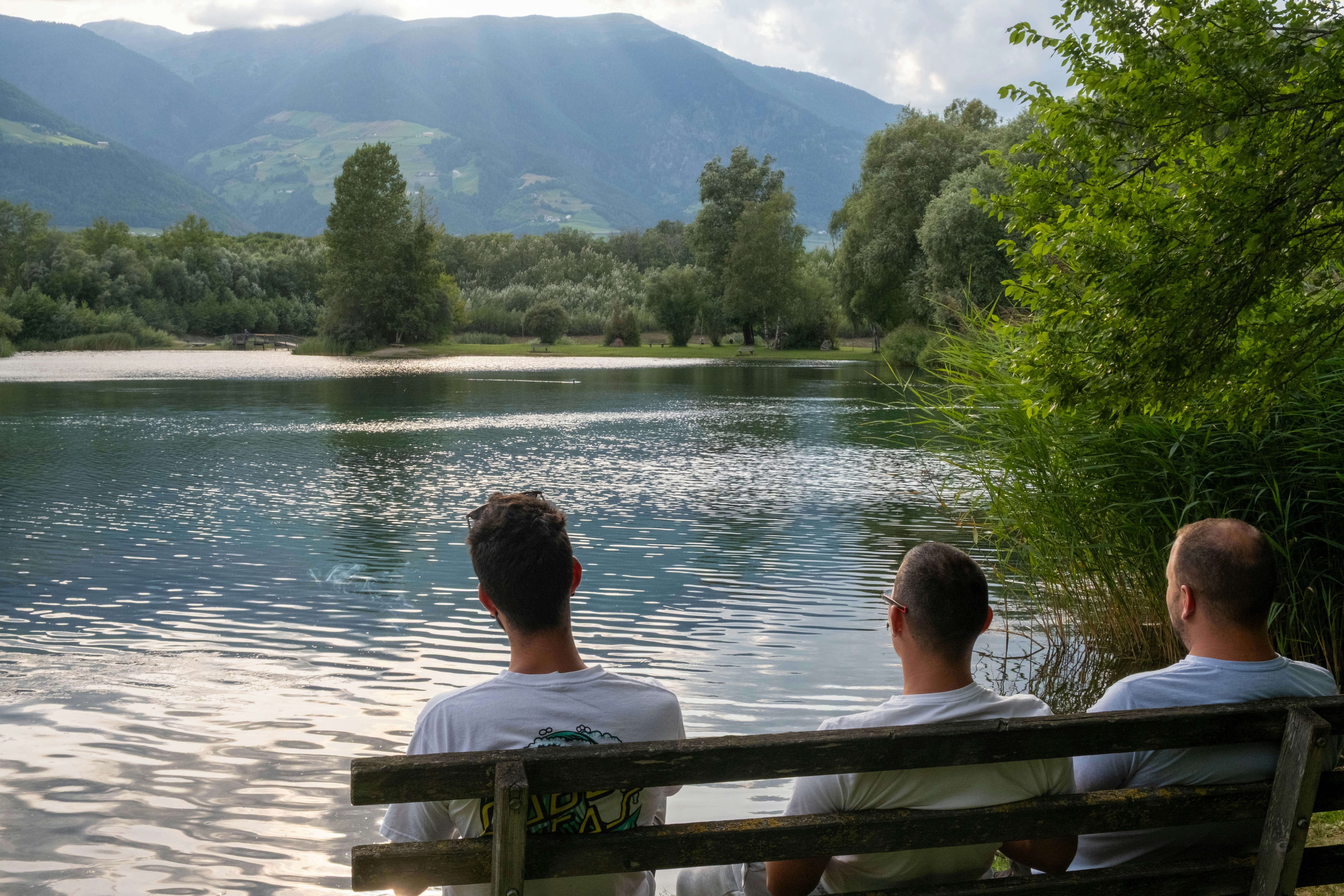 Drei Männer sitzen auf einer Bank an einem See.
