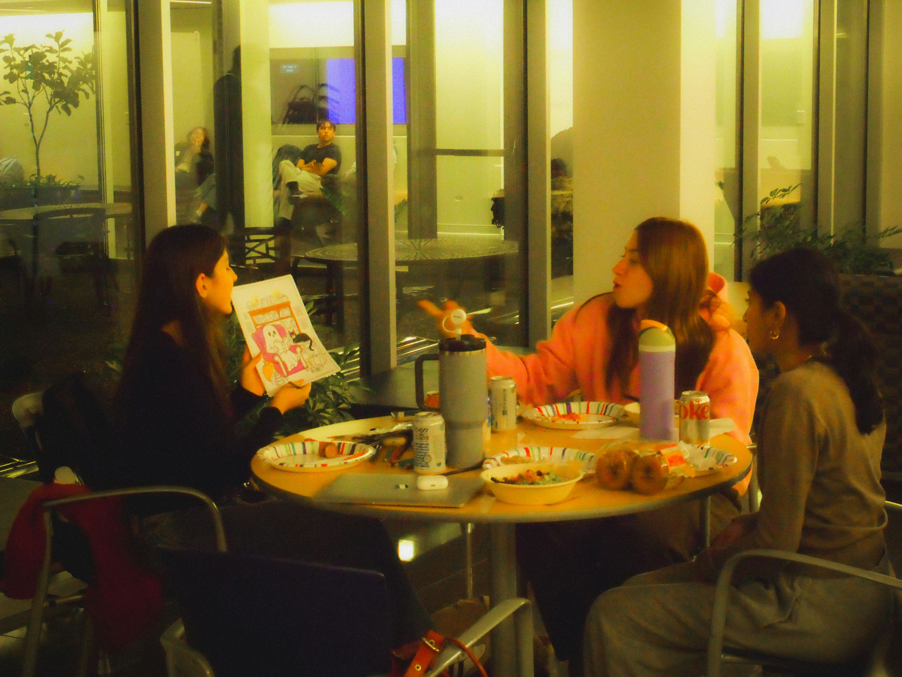 Three women talking at a table with snacks.