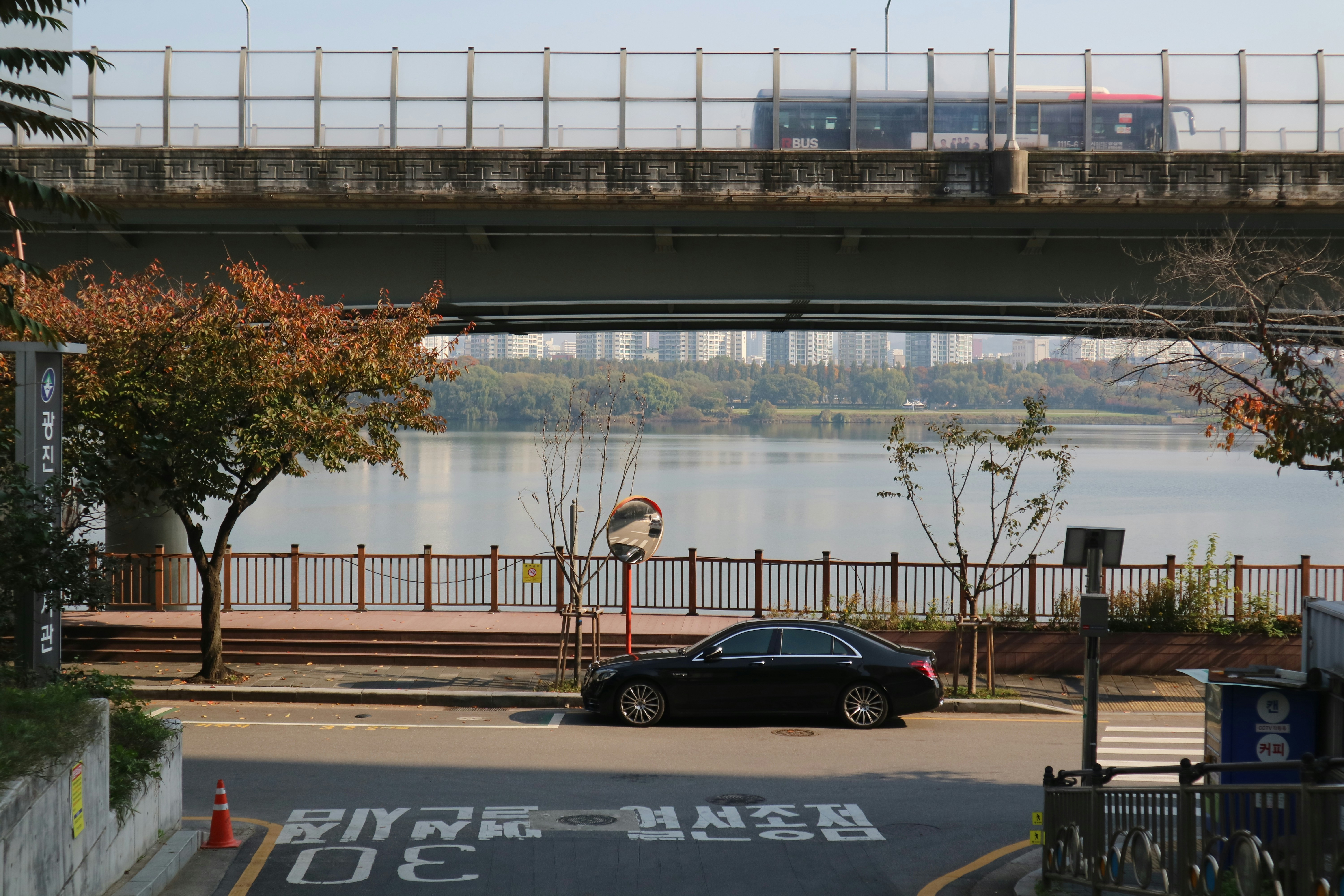 Black car parked by river with bridge and city background