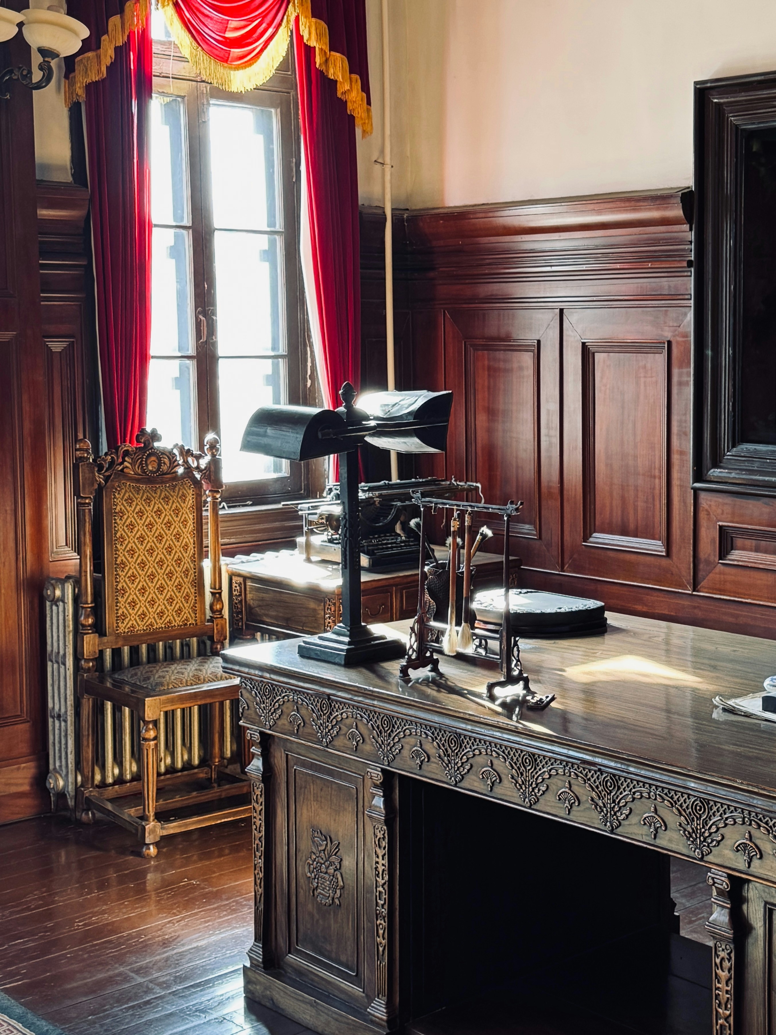 Ornate wooden desk with lamp and antique chair.