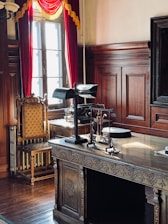 Ornate wooden desk with lamp and antique chair.