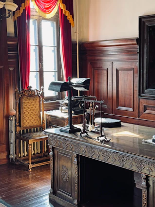 Ornate wooden desk with lamp and antique chair.