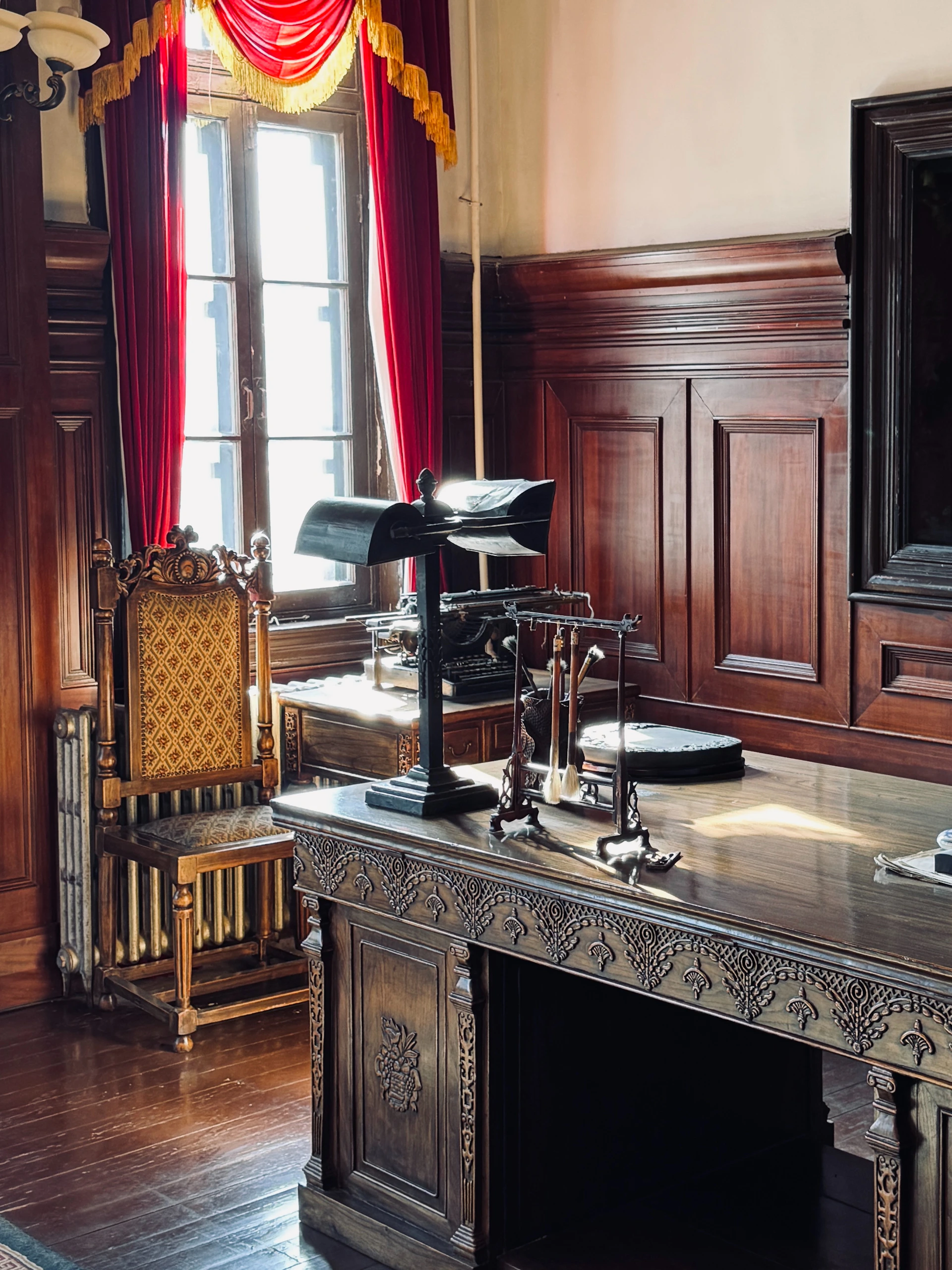 Ornate wooden desk with lamp and antique chair.