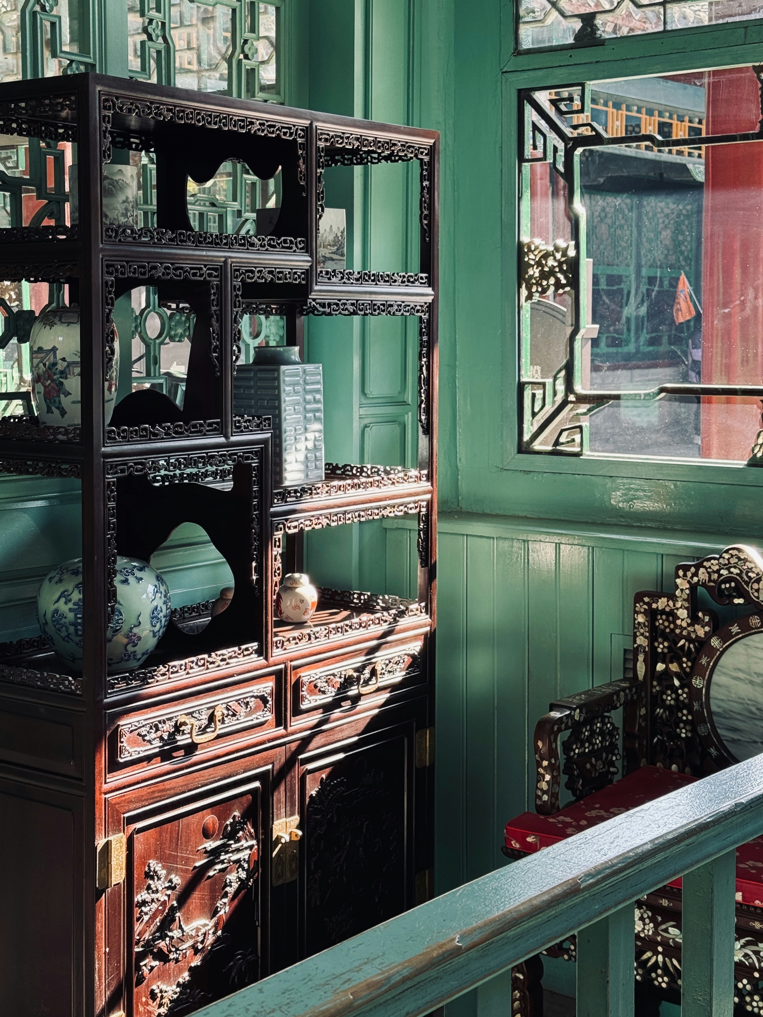 Ornate wooden cabinet with decorative vases and chair.