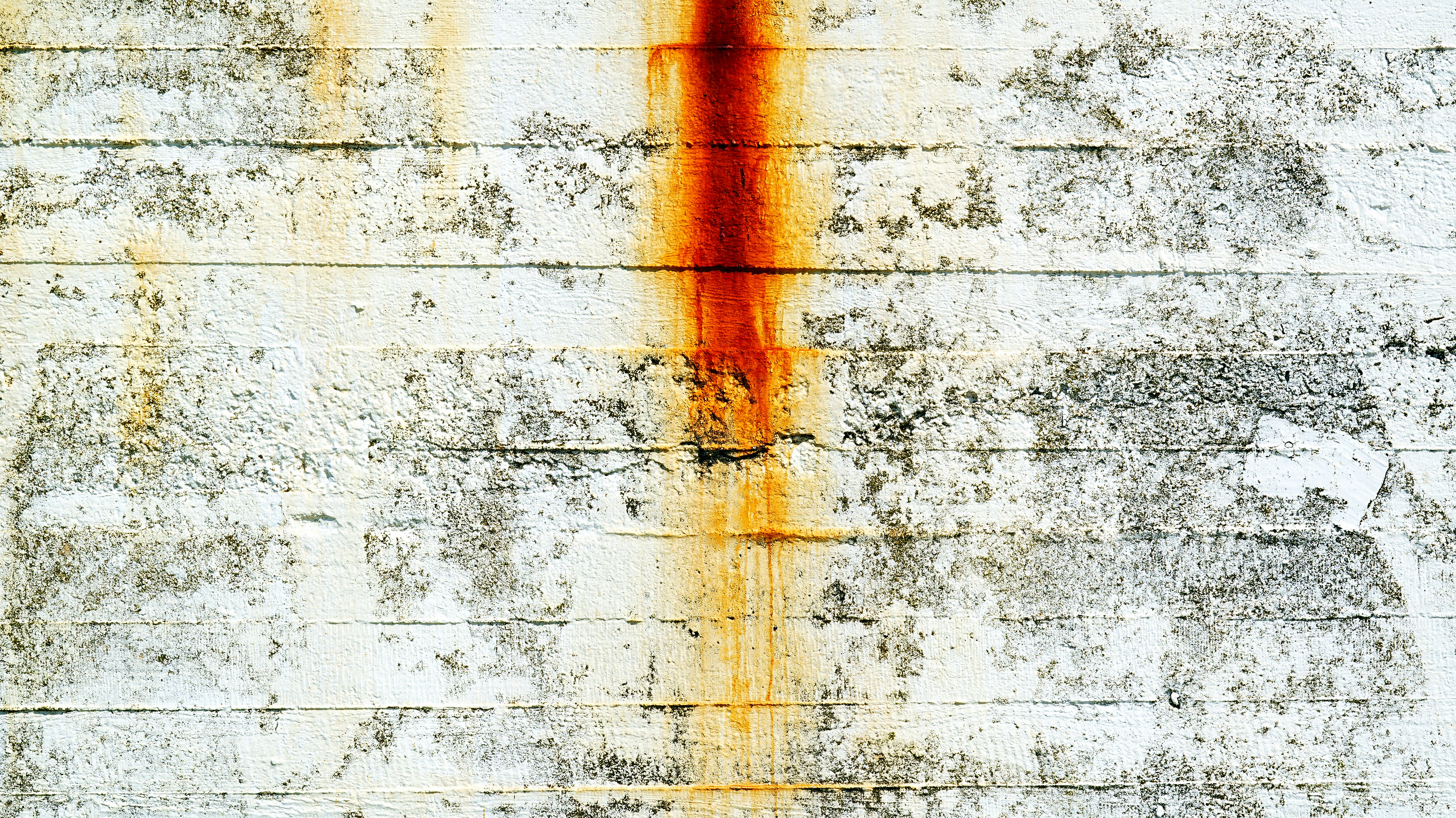 Weathered concrete wall with orange rust streaks