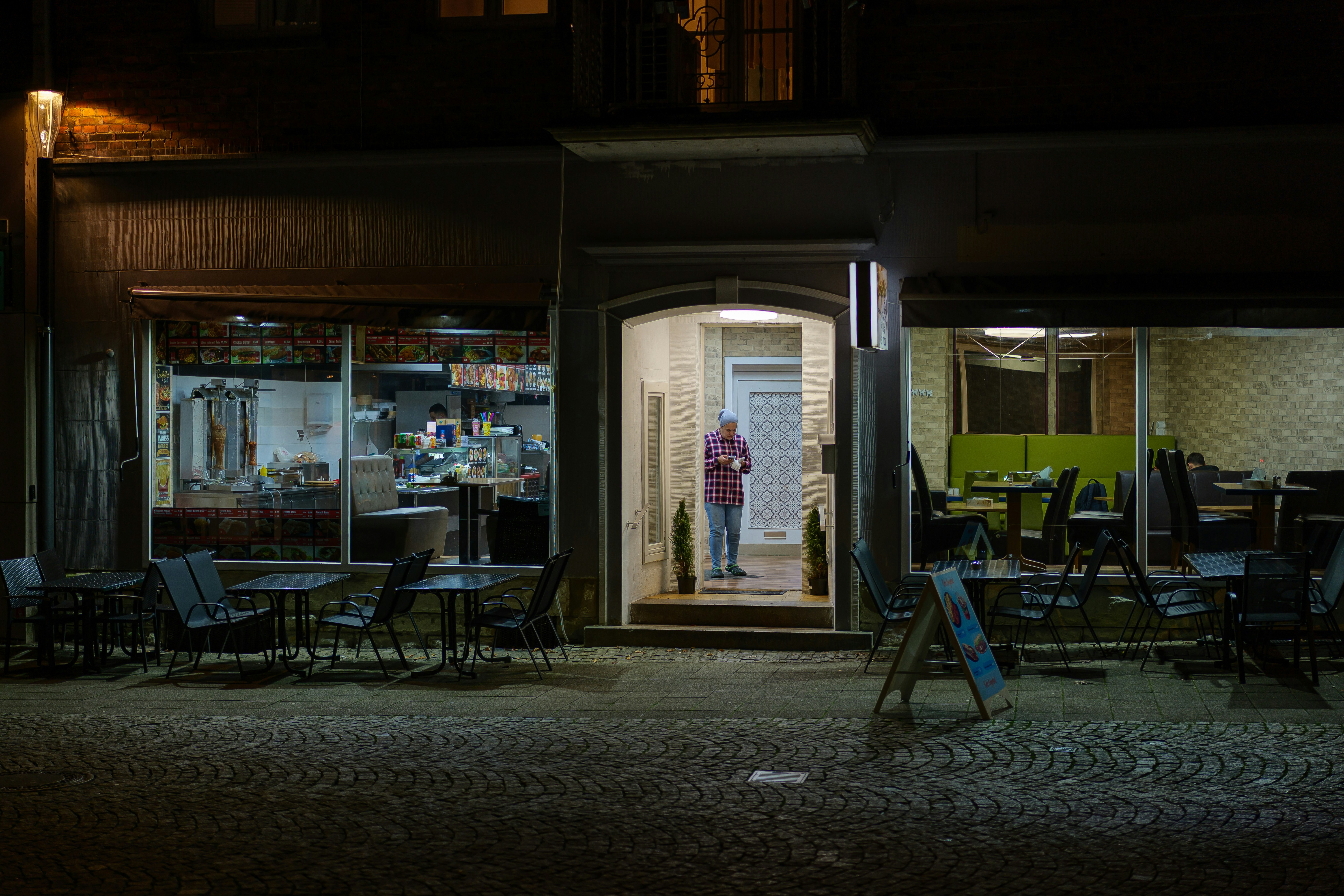 Person standing in doorway of a restaurant at night.