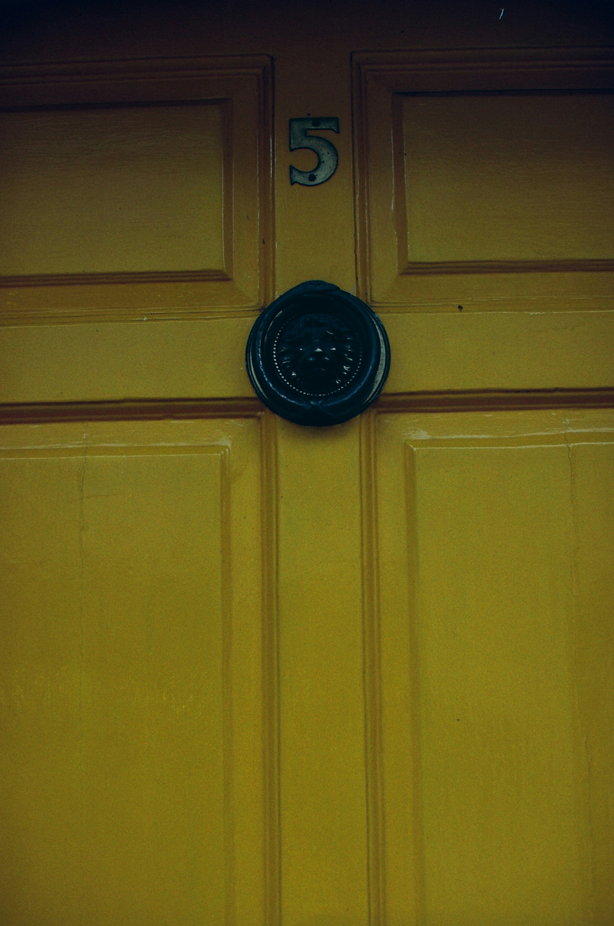 Puerta amarilla con número cinco y pomo negro.