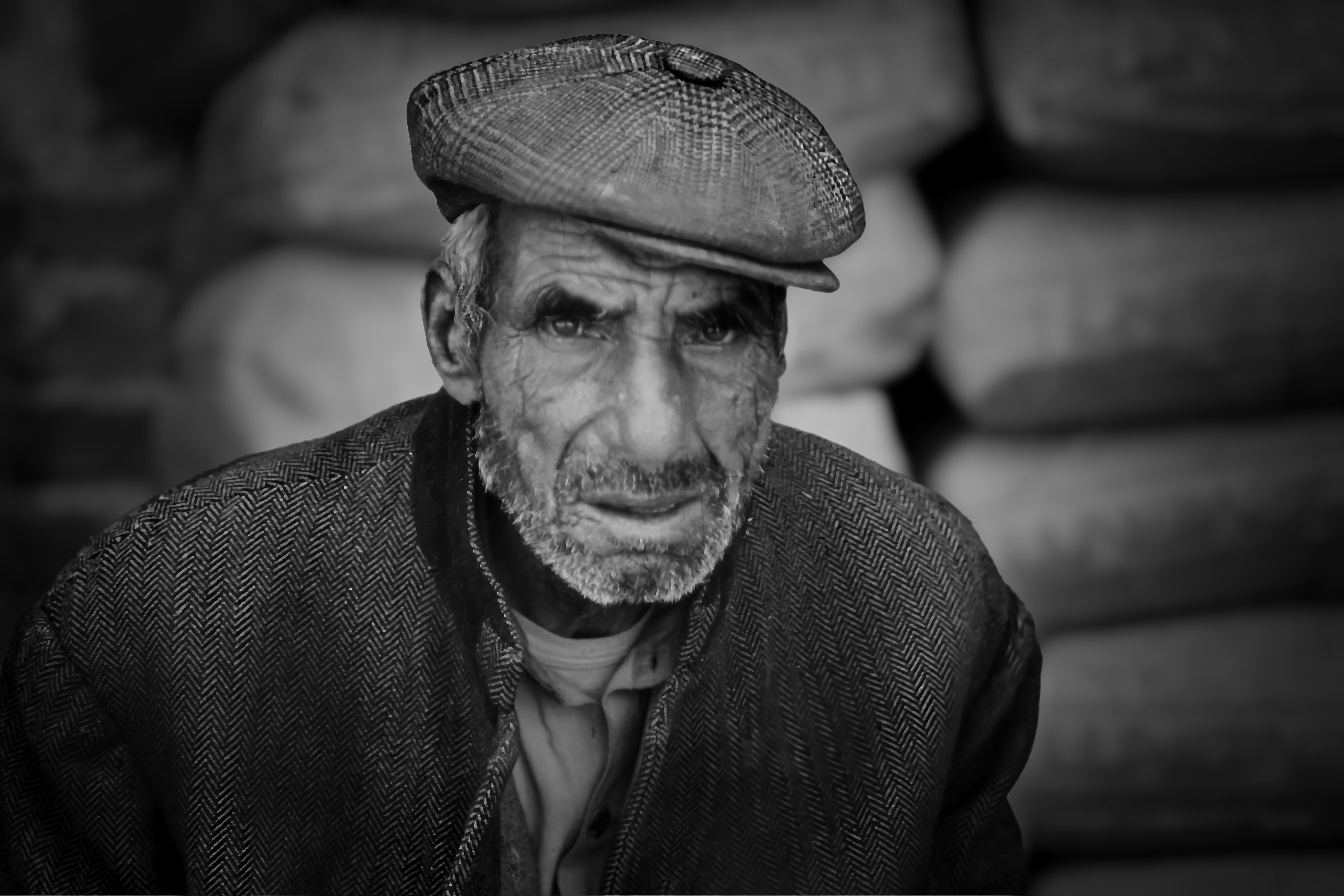 An elderly man wearing a flat cap looks forward.