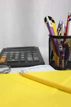 Desk with calculator, pens, and yellow envelope.