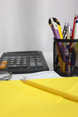 Desk with calculator, pens, and yellow envelope.