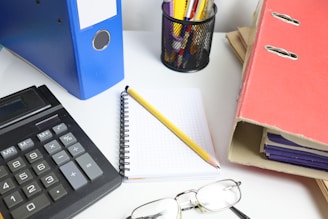 Desk with calculator, binders, notebook, and glasses